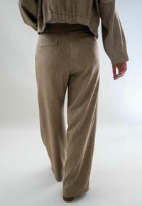 Bruine, wijde broek gemaakt van gestructureerde stof, met een subtiel patroon en achterzakken voor detail.