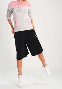 Grijs-roze hoodie met voorzakken, gecombineerd met zwarte korte broek met een Adidas-logo en witte hoge sneakers.