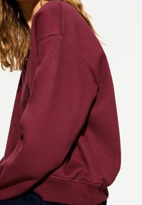 Vinröd sweatshirt med rund halsringning, ribbade muddar och fåll. Mjuk, strukturerad tyg med avslappnad passform.