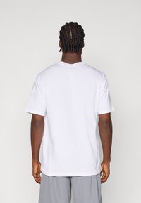 Witte katoenen t-shirt met korte mouwen, ronde halslijn en een relaxte pasvorm, gezien vanaf de achterkant, gepresenteerd tegen een effen achtergrond.