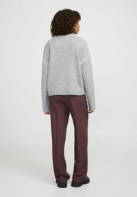 Pull en tricot gris à coupe décontractée, avec des détails de couture subtils et des poignets côtelés, associé à un pantalon bordeaux et des chaussures noires.