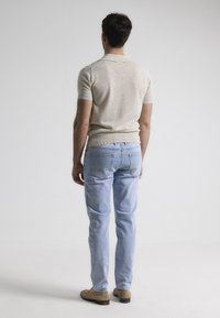 Camisa polo de manga corta beige y jeans de color azul claro. La camisa presenta detalles acanalados y un cuello clásico. Unos zapatos de ante claros completan el conjunto.