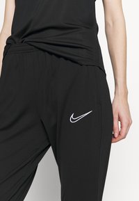 Schwarze Jogginghosen mit elastischem Bund, Seitentaschen und einem weißen Nike-Logo auf dem linken Oberschenkel. Glattes, leichtes Material.