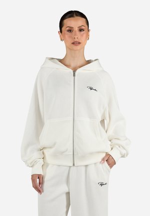 Felpa con zip bianca a coste, dotata di un ampio cappuccio, tasche frontali e logo ricamato nero. Tessuto morbido, vestibilità comoda e polsini elasticizzati.