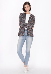 Cardigan floral cu un fundal negru, flori colorate, cu deschidere în față, mâneci lungi, asortat cu blugi ușor albaștri și adidași albi.
