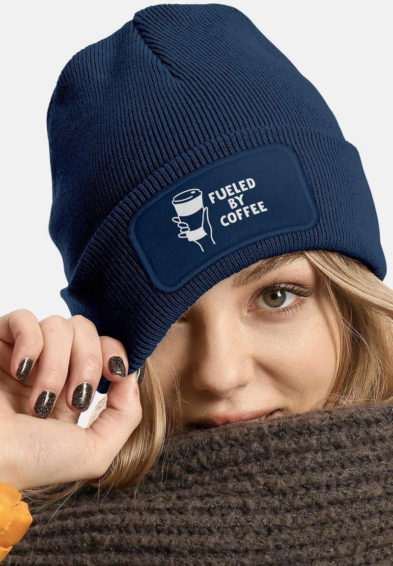 Navy knit beanie with a fabric patch displaying "FUELED BY COFFEE" and an image of a coffee cup. Text is in white. Soft texture.
