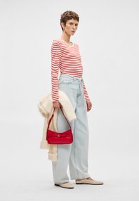 Ριγέ κόκκινη και λευκή μπλούζα με μακριά μανίκια, ανοιχτό μπλε ψηλόμεσα τζιν, κρεμ υπερμεγέθη πουλόβερ, κόκκινη τσάντα και μπεζ μπαλαρίνες.