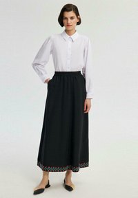 Cămașă albă cu mâneci lungi și nasturi, combinată cu o fustă neagră cu talie înaltă, decorată cu broderie florală colorată la tiv. Pantofi cu talpă joasă negri.