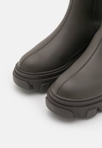Botas de tobillo de cuero gris con puntera redondeada, suelas de goma texturizada y detalles de costura visibles a lo largo de las costuras.