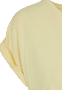 Gul kortærmet t-shirt med rund halsudskæring, blødt stof og rullekant-detalje. Glat tekstur uden synlige mønstre eller accenter.