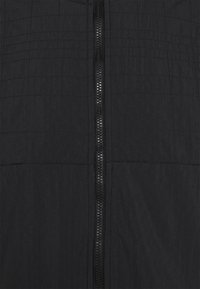 Černá zipová bunda s prošívanou texturou, která obsahuje přední zip a vodorovné švy. Materiál se zdá být lehký a odolný.