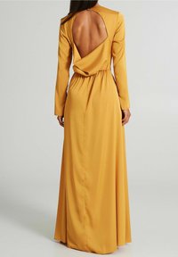 Gul långärmad klänning med draperad rygg, öppen utskärning, elastisk midja och mjuk tyg. Golv-lång med lös passform.