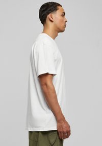 Tricou alb din bumbac, cu o croială lejeră, mâneci scurte și gât rotund. Textură netedă, detalii pe cusăturile laterale și fără logo-uri vizibile.
