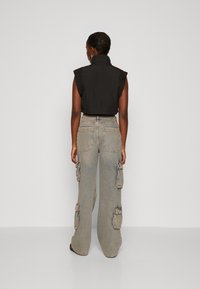 Svart croppad topp med volangärmar som är kombinerad med ljusblå cargobyxor med stora fickor och vida ben, sedd bakifrån.