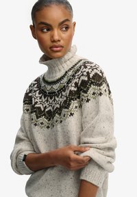 Gebreide pullovertrui in lichtgrijs met een hoge kraag, voorzien van een geprinte schouderpartij in zwart en groen, en opgerolde mouwen met subtiele spikkels.