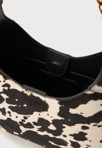 Borsa a spalla in pelle di vitello bianca e nera con una superficie texture e un interno in pelle nera elegante. Presenta una chiusura a pressione.