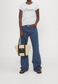 Camiseta blanca de manga corta con logo de "Armani Exchange", combinada con jeans azules de pierna ancha y un bolso de paja de dos tonos y negro. Chanclas negras.