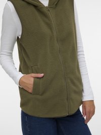 Φυστικί πράσινο, αμάνικο γιλέκο από φλις με φερμουάρ μπροστά και κουκούλα. Διαθέτει πλαϊνές τσέπες και απαλό, υφή επιφάνειας.