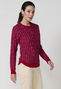 Sweater rouge en maille avec un motif à carreaux texturé. Présente un col rond et des poignets côtelés. Accentué de fils bleus tout au long.