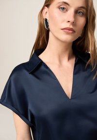 Bluză din satin de culoare bleumarin, cu mâneci scurte și decolteu în V, având o textură fină și un guler bine definit pentru un aspect rafinat.