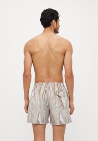 Shorts de bain présentant un motif ondulant beige clair et marron, fabriqués dans un tissu à texture douce ; taille élastique avec une poche arrière.
