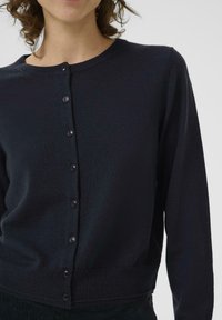 Schwarze Strickjacke mit langen Ärmeln, rundem Ausschnitt und Knopfverschluss auf der Vorderseite. Glatte Textur und taillierte Passform.