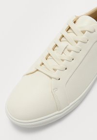 Baskets en cuir blanc avec lacets plats, bout rond et finition texturée. Présentent des coutures sur les côtés et une semelle en caoutchouc.