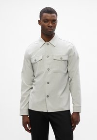 Γκρι πουκάμισο με γιακά και δύο τσέπες στο στήθος. Φτιαγμένο από ελαφρύ ύφασμα, διαθέτει καθαρή σχεδίαση και κανονική εφαρμογή.