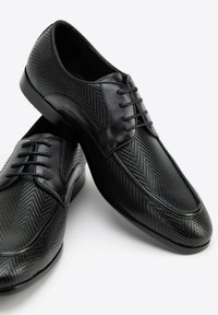 Scarpe eleganti in pelle nera con un motivo a zig-zag texturizzato, chiusura con lacci, punta rotonda e una finitura liscia e lucidata.