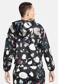 Veste à capuche en tissu lisse, avec un fond noir et des motifs de roches abstraits colorés. Design court et poignets élastiques.