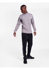 Grijze ritssluiting lange mouwen top met zwarte accenten, gecombineerd met zwarte trainingsbroek met een chevronpatroon langs de zijkanten en zwarte sneakers.