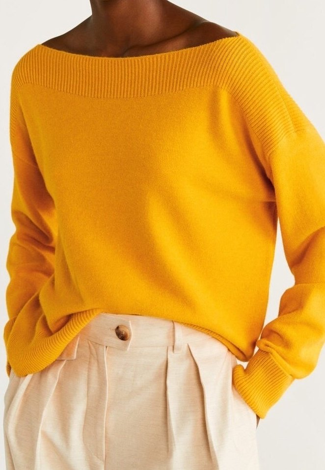 Leuchtend gelber Pullover mit weitem, geripptem Ausschnitt und langen Ärmeln. Weiche Textur und lockere Passform, kombiniert mit hellen, hoch taillierten Hosen.