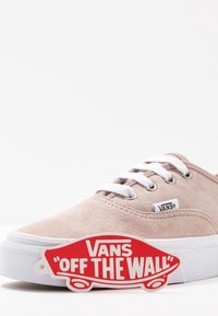 Sneaker Vans in suede marrone chiaro con lacci e suola bianchi, dotata di etichetta rossa con il logo skateboard "Off The Wall" di Vans nella parte anteriore.