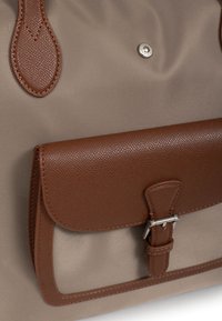 Borsa tote in tessuto beige con un flap e una tracolla in pelle marrone testurizzata, caratterizzata da un gancio in argento e dettagli in pelle marrone.