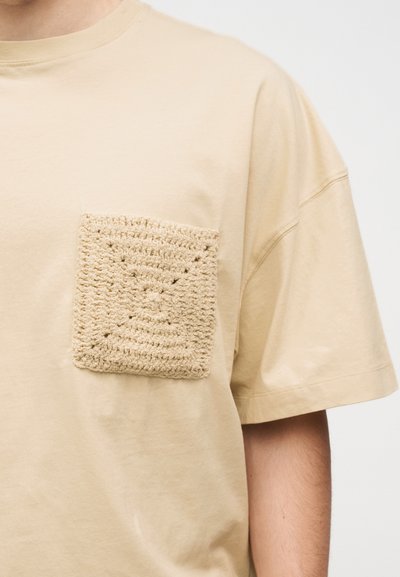 Μπεζ T-shirt με υπερμεγέθη μανίκια που διαθέτει υφασμένη, πλεκτή τετράγωνη τσέπη στο αριστερό στήθος.