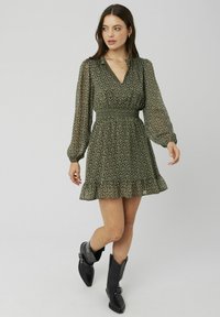 Robe florale verte avec de longues manches transparentes, taille froncée et ourlet à volants. Assortie à des bottes noires à bout pointu. Texture de tissu léger.