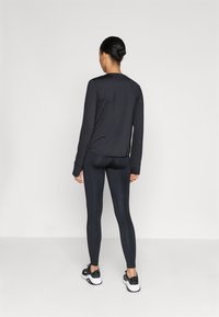 Black long-sleeve top paired with dark leggings. Features soft fabric, fitted design, and a crew neck. Flat seams with no visible patterns.