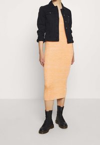 Svart denimjacka, ribbat orange klänning, knälång, och svarta snörboots med gummisula. Enkelt, strukturerat design genomgående.