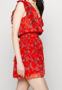Rotes Blumenkleid mit gerüschten Ärmeln, gestuftem Design und blauen Akzenten. Aus leichtem Stoff gefertigt, mit taillierter Taille und lockeren Saum.