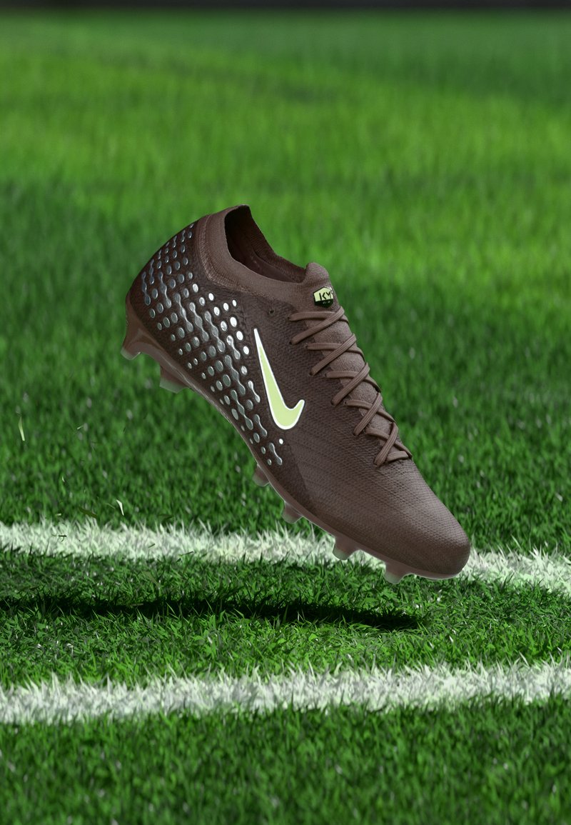 Rudas futbolo batelis su baltu logotipu ir tekstūruotomis šoninėmis pusėmis, sklendžiantis virš žalios žolės lauko netoli baltos ribinės linijos.