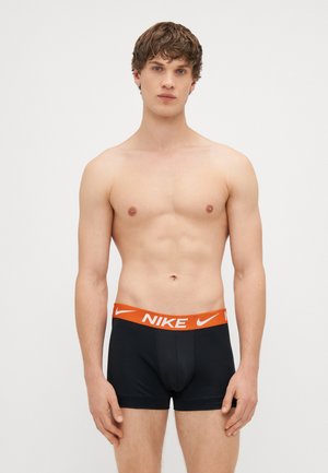 Fekete boxerral van ellátott alsónadrág vastag narancssárga Nike logóval a derékpántján, sima anyagból készült, testhezálló kialakítással és látható minták nélkül.