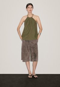 Oliwkowy top na halter z plisowanym wzorem, w połączeniu z brązowymi zamszowymi kulotami. Modelka nosi czarne klapki i srebrną bransoletkę.