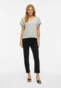 Top in maglia leggero beige con righe blu, scollatura a V e maniche corte, abbinato a pantaloni neri slim fit e scarpe aperte nere.