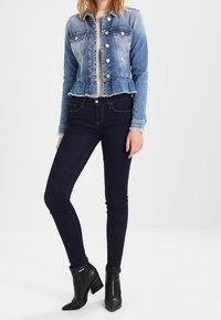 Jeansjacka med en ljus och mörkblå tvätt, figurnära stil och fransad nederkant; tillsammans med mörka skinny jeans och svarta klackade ankelskor.