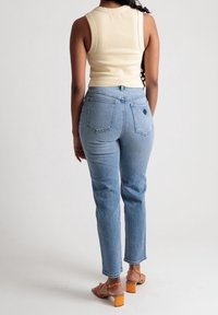 Beige ilmanhihaisia yläosa, vaaleansiniset korkeavyötäröiset farkut takataskuilla ja ruskeat sandaalit paksulla oranssilla korkolla. Suorat pinnat.