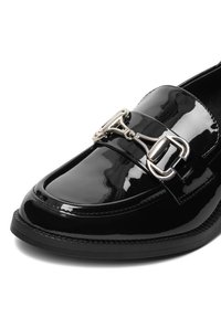 Czarny lakierowany mokasyn z zaokrąglonym noskiem, ozdobiony srebrną klamrą na cholewce oraz teksturowaną czarną podeszwą.