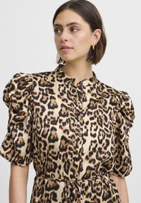 Leopardenmuster Bluse in Beige und Schwarz, mit gepufften Kurzärmeln, einer durchgehenden Knopfleiste und einer taillierten Passform mit einem Bindeband.