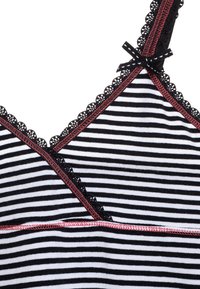Tessuto a strisce bianche e nere con un intricato bordo in pizzo nero lungo il décolleté, accentuato con cuciture rosse e un dettaglio a fiocco.