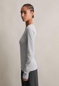 Szürke, hosszú ujjú felső, testhezálló kialakítással és puha tapintással, sötét szoknyával párosítva. Az ing ujj végén hüvelykujjtartókkal rendelkezik.