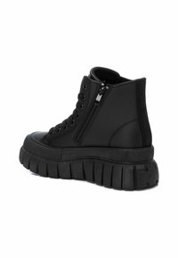 Zapatillas altas negras con una suela gruesa y estriada. Las características incluyen un sistema de cordones en la parte delantera y una cremallera lateral, fabricadas en material sintético suave.